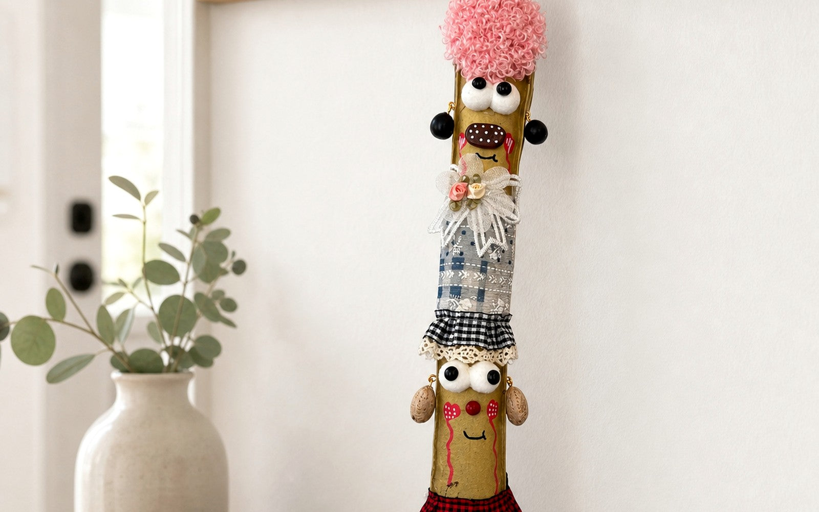Muñeca de Frijol Espada de YUNOVA colgada en un gancho de pared junto a un jarrón cerámico